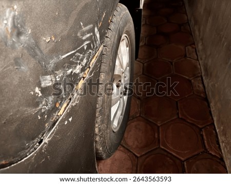black car side damage. Sharp scratches and peeling paint areas give a rough and worn look. Can be used for damage concepts, problems, or repair needs. The dark background adds drama.