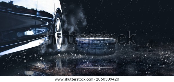 The black car spare wheel is\
placed on the road in the downpour, copy space on black\
background