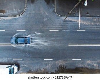 Black Car Splashes Through Large Puddle On Flooded Street. Aerial Photo