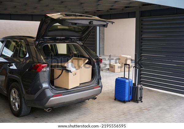 Black\
car in yard with open trunk and boxes for\
moving
