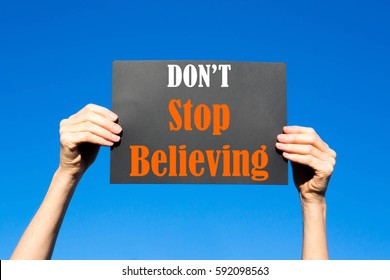 Black card placard with the concept of Don't Stop Believing against a clear blue sky background