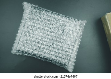 Black Cardboard Box Wrapped In Bubble Wrap On A Black Background.