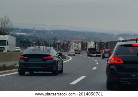 Black cars on autobahn in cloudy day with city background 