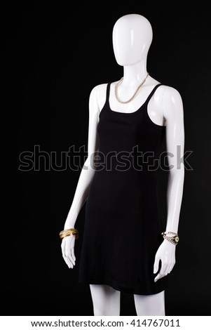 Black casual dress with accessories. Mannequin wearing simple dark dress. Woman's casual evening look. Gold bracelet and dark garment.