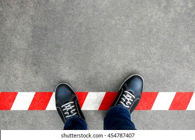 Black casual shoes standing on red and white line. Crossing the limit. Disobey and act against the rule.