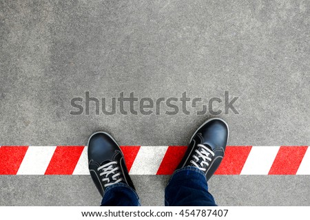 Black casual shoes standing on red and white line. Crossing the limit. Disobey and act against the rule.