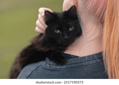 black cat sits on owner shoulder in park in summer - Powered by Shutterstock