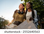 Black and caucasian young female tourists have fun hugging and holding a city map laughing and looking into the distance with sun flares peeking through from behind