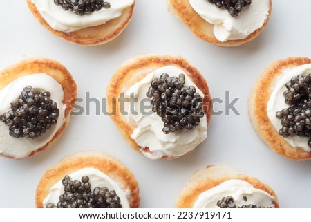 Black caviar appetizers, mini pancakes with cream, seafood for holiday, Horizontal close up, macro pattern on a white background