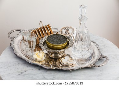 Black caviar on ice in silver bowl, Vodka and bread on white marble table