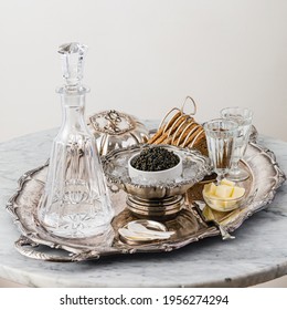 Black caviar on ice in silver bowl, Vodka and bread on white marble table