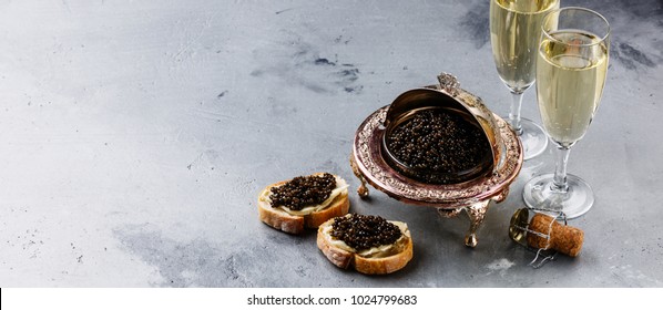 Black caviar in silver bowl, sandwiches and champagne on gray concrete background copy space