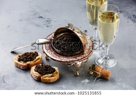 Black caviar in silver bowl, sandwiches and champagne on gray concrete background
