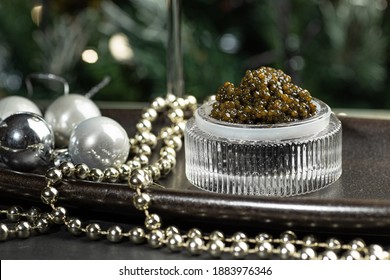 Black caviar. Black sturgeon caviar in a cut-glass bowl, a glass of champagne and silver beads on a silver tray.