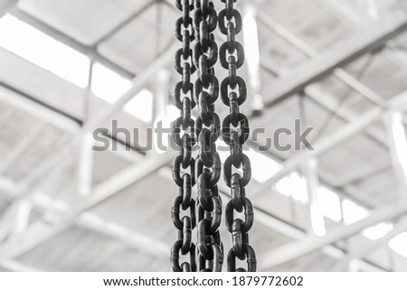 Black chain with iron links of the lifting mechanism of an overhead crane against the background of an industrial workshop or factory