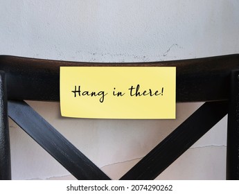 Black Chair Back With Note Written HANG IN THERE, Positive Self Seminder To Remain Persistent And Determined In Difficult Circumstances, Encouragement Note Telling Someone To Not Give Up In Difficulty