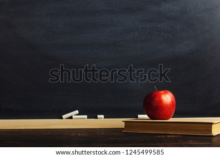 Black chalk board over wooden table with a book and an apple, blank for text or background for a school theme.