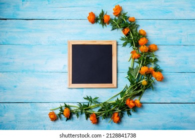 Black Chalkboard Wooden Square Frame Mockup With Globeflowers On The Blue Table. Empty Blackboard Frame Mock Up For Presentation Design. Template Black Felt Letter Board Framing For Modern Art.