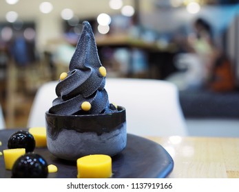 A Black Charcoal Soft Serve Ice Cream Topped With Yellow Sugar Flake. Healthy Dessert With Selective Focus.