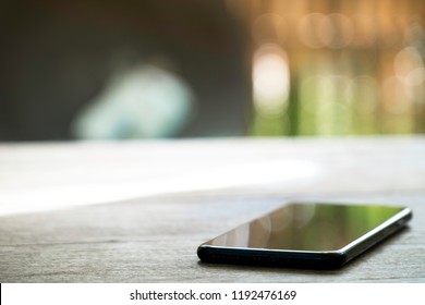 black charging mobile phone on the wooden table on blured nature background.