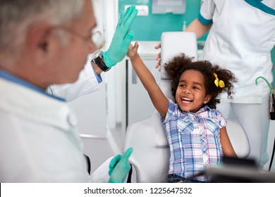 Black cheerful young girl in dental chair making joke with male dentist