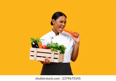 Black Chef Woman Holding Wooden Crate With Organic Vegetables And Biting Carrot, Cheerful African American Cook Lady Enjoying Tasty Fresh Ingredients For Cooking, Standing On Yellow Background - Powered by Shutterstock