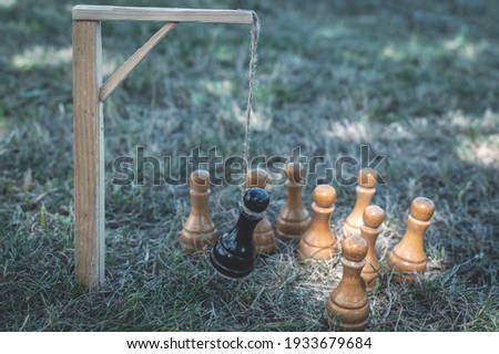 The black chess pawn is executed and hangs on the gallows in the noose and around the white pieces. Metaphor, the concept of reprisal, persecution, repression, execution of the enemy, betrayal