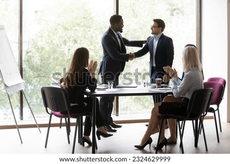 Black chief ceo shaking hand of millenial european worker manager welcoming or thanking for good job while staff applaude, happy young businessman is awarded by boss in presence of colleagues