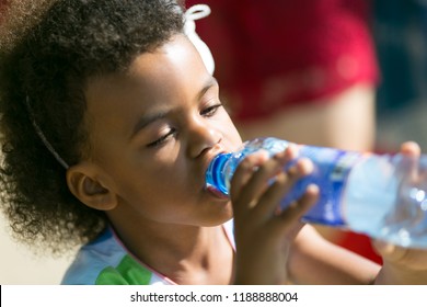 A Black Child Eagerly Drinks Water From A Bottle. A Little Girl Keeps A Thirst Out Of A Plastic Bottle On A Hot Day.