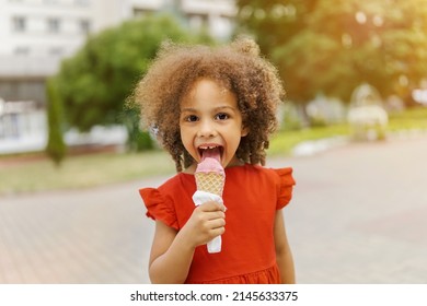 A Black Child Eats Ice Cream On A Hot Day. Ice Cream In A Waffle Cone. A Happy And Contented Child In A Red Dress At Summer.