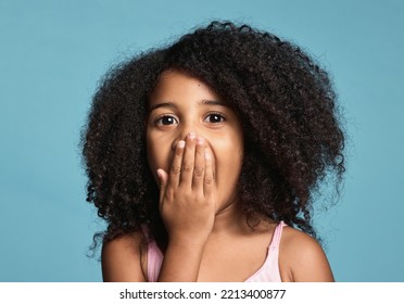 .Black Child, Surprised And Shocked With Wow Expression Covering Mouth In Awe Feeling Positive And Excited With Natural Afro Hair. Face Portrait Of Cute Kid Amazed And Happy Against Blue Background.