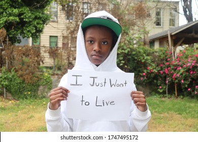 Black child wearing hat and hoodie holding sign with words I Just Want To Live written on it standing outdoors