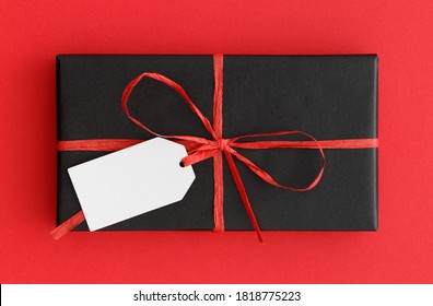 Black Christmas Gift With A Blank Tag Mockup On A Red Background.