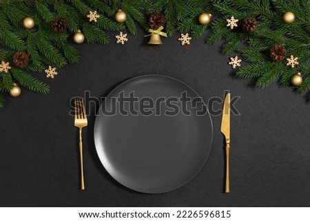 Black Christmas table setting with golden festive decor and fir branches. New Year serving with empty black plate. Copy space, top view, flat lay.
