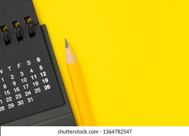 Black Clean Calendar With Yellow Pencil On Solid Yellow Background With Copy Space Using As Reminder, Schedule Or Business Project Plan And Timeline Concept.