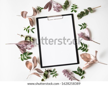 Black clipboard, white paper for text and creative frame composition of various painted leaves and green leaves on white background. Top view. Copy space