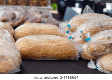 Black cloth on a table at a farmer's market.There are multiple loaves of homemade crusty flaxseed bread in clear plastic bags with blue tags. The sweet crusty bread is golden color with dark seeds. - Powered by Shutterstock