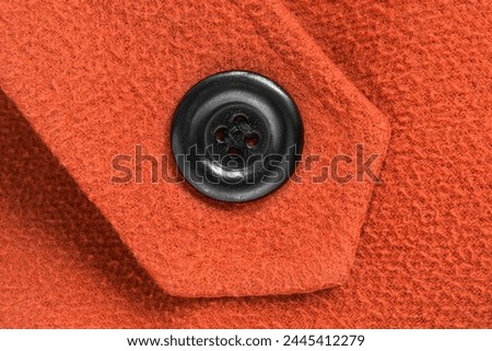 Black clothes button sewn on orange color wool background