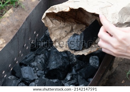 Black coal as natural fuel for cooking barbeque in brazier. Hand holds paper bag with charcoal 