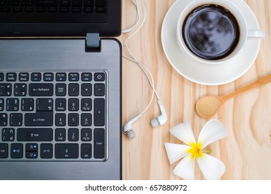 Black Coffee And Computer Notebook Or Laptop With In-ear Headphone, Plumeria Flower On Wooden Background.