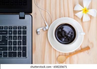 Black Coffee And Computer Notebook Or Laptop With In-ear Headphone, Plumeria Flower On Wooden Background.