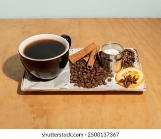 A black coffee cup with cinnamon sticks, milk, coffee beans, and a slice of orange on a rustic tray atop a wooden surface, creating a cozy coffee scene. - Powered by Shutterstock