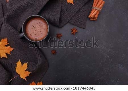 Black coffee cup, yellow maple leaves, spices, grey scarf on dark grey background. Copy space, top view. Autumn background, fall season, thanksgiving, coffee shop menu concept.
