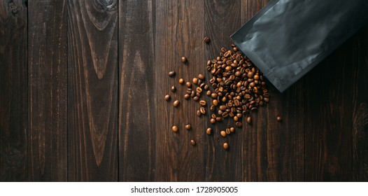 Black Coffee Foil Packaging Bag On Wooden Table Top View. Spilled Beans Flat Lay Concept. Room For Text.