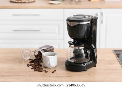 Black coffee machine with cup and jar of beans on counter in kitchen