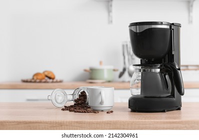 Black coffee machine with cup and jar of beans on counter in kitchen