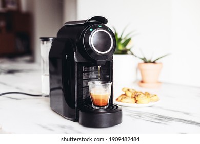 Black coffee machine making espresso on a marble table. White kitchen, plants, cinnamon buns on the background