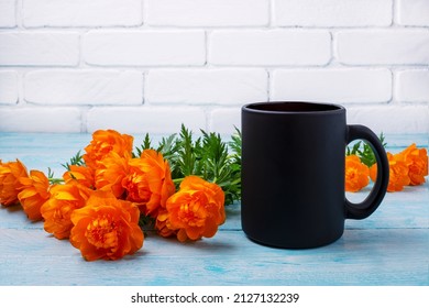 Black Coffee Mug Mockup With Orange Globeflowers On The Blue Table. Empty Mug Mock Up For Brand Promotion