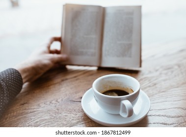 Black coffee on saucer with Human hand holding vintage book on blurred background on the wooden table next to big coffee shop window. - Shutterstock ID 1867812499