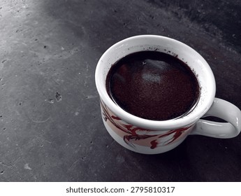 Black coffee in white patterned ceramic mug on dark concrete surface. Traditional cup design, rustic table background, hot beverage